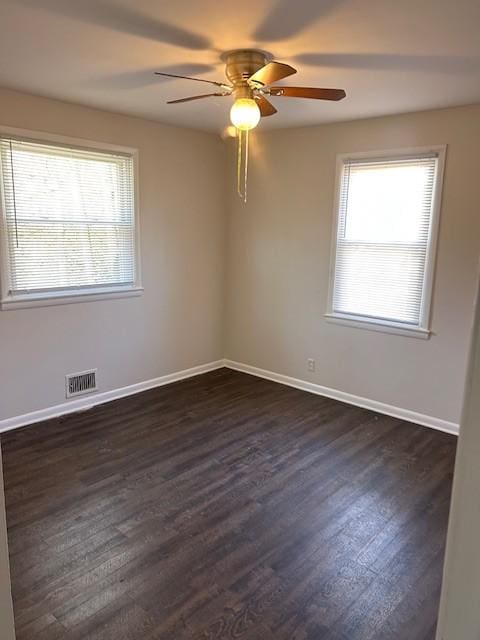 spare room with dark wood-type flooring, a ceiling fan, visible vents, and baseboards