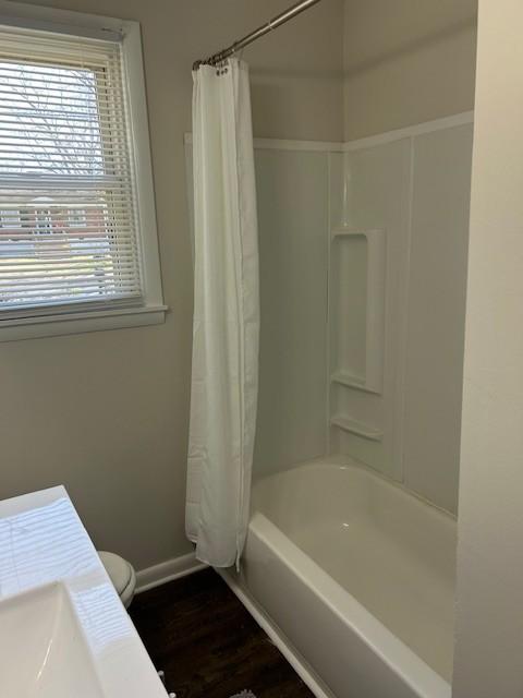 full bath with baseboards, wood finished floors, toilet, and shower / tub combo with curtain