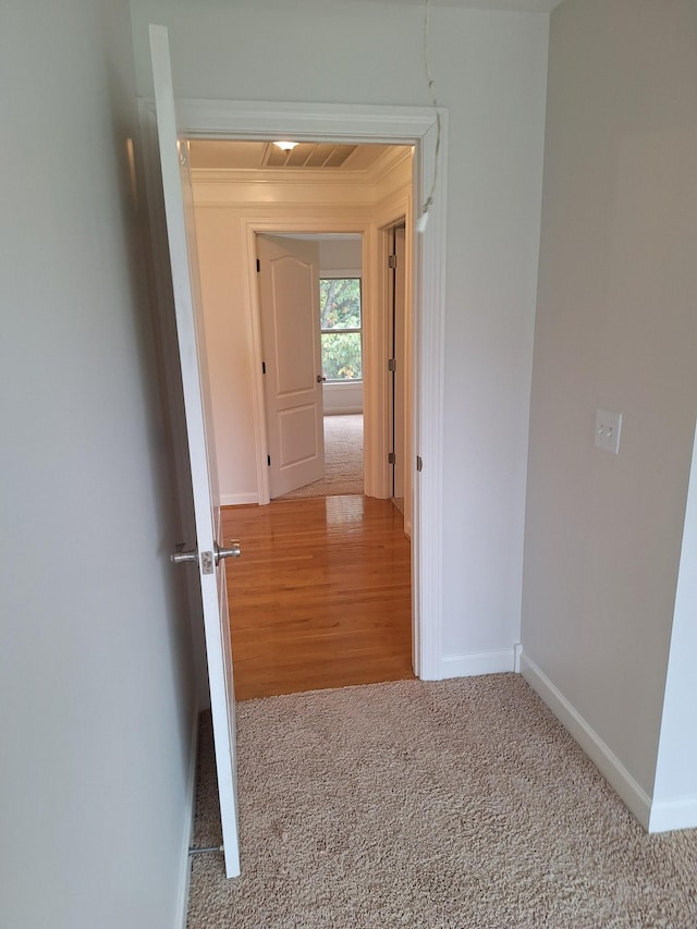 corridor featuring carpet floors, ornamental molding, visible vents, and baseboards