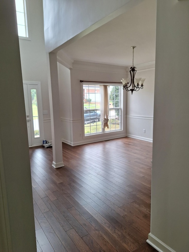 interior space with dark wood-style flooring, a wainscoted wall, crown molding, and an inviting chandelier