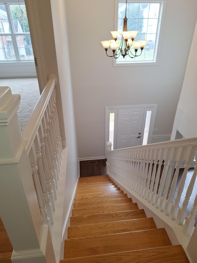 stairs with baseboards, wood finished floors, a towering ceiling, and a notable chandelier