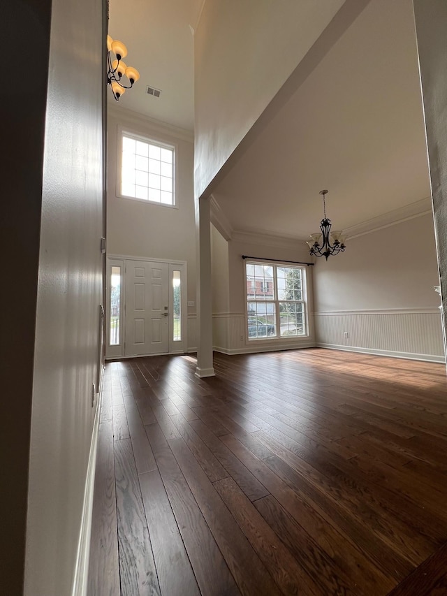 foyer entrance with an inviting chandelier, visible vents, ornamental molding, and dark wood finished floors