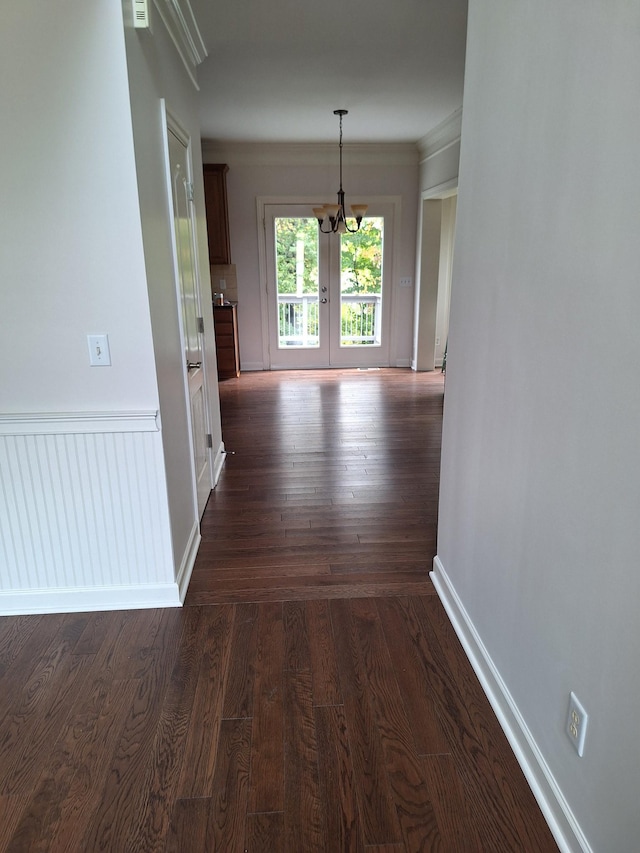 corridor featuring dark wood-style floors, a chandelier, ornamental molding, and baseboards