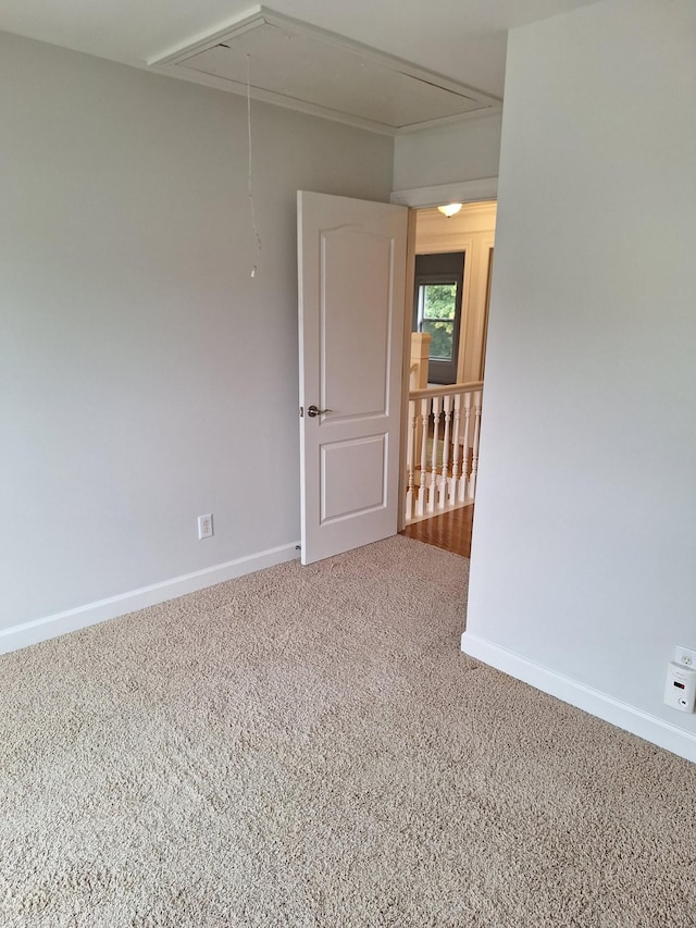 carpeted empty room featuring attic access and baseboards