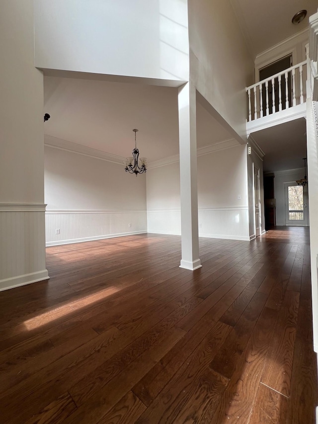 interior space featuring a wainscoted wall, crown molding, a towering ceiling, an inviting chandelier, and dark wood-type flooring