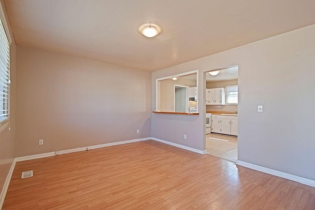 empty room featuring light wood-style flooring, a sink, visible vents, and baseboards