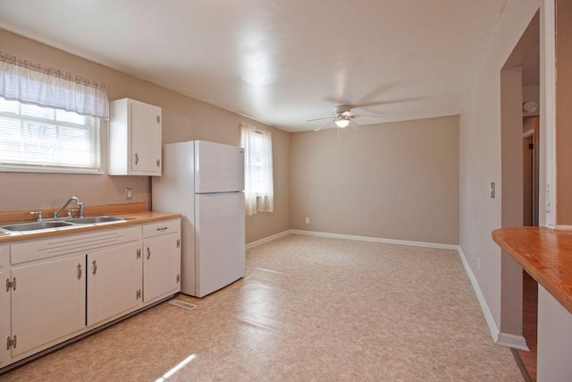 kitchen featuring baseboards, white cabinetry, a sink, and freestanding refrigerator