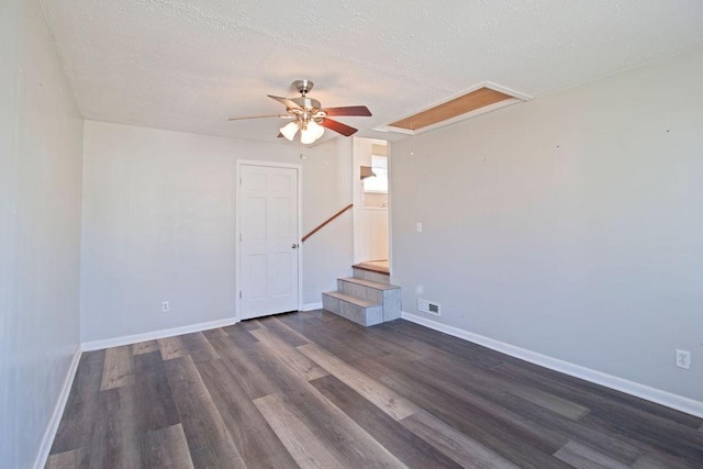 unfurnished room featuring a textured ceiling, visible vents, baseboards, dark wood-style floors, and attic access