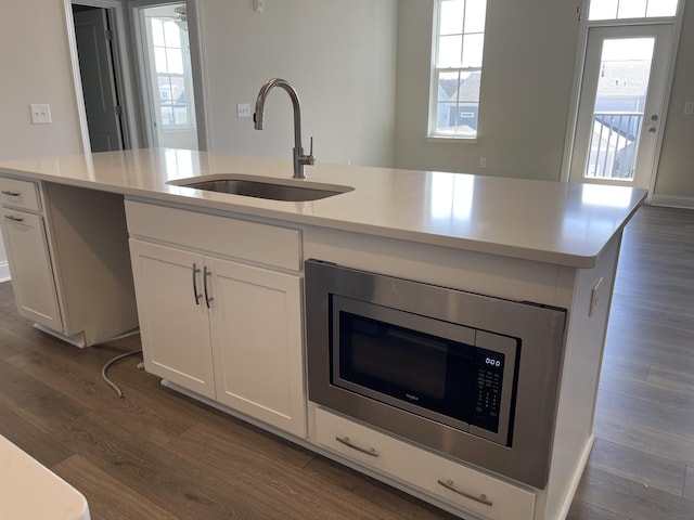 kitchen with dark wood-style floors, a center island with sink, stainless steel microwave, and a sink