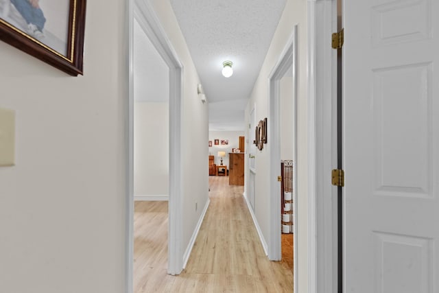 hallway with light wood-type flooring, baseboards, and a textured ceiling