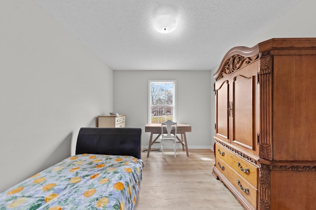 bedroom featuring baseboards, a textured ceiling, and light wood finished floors