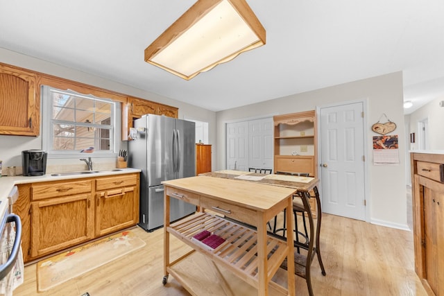 kitchen with freestanding refrigerator, light countertops, a sink, and light wood finished floors