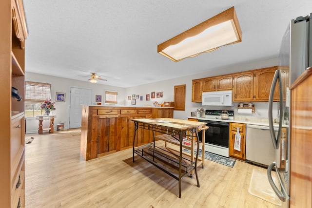 kitchen with light wood finished floors, brown cabinetry, ceiling fan, appliances with stainless steel finishes, and light countertops