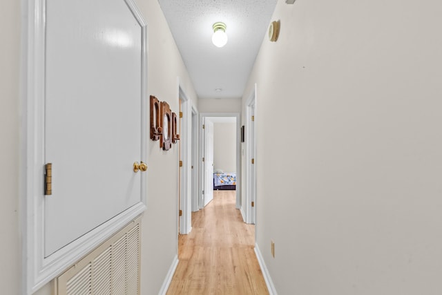 hall with baseboards, a textured ceiling, and light wood finished floors