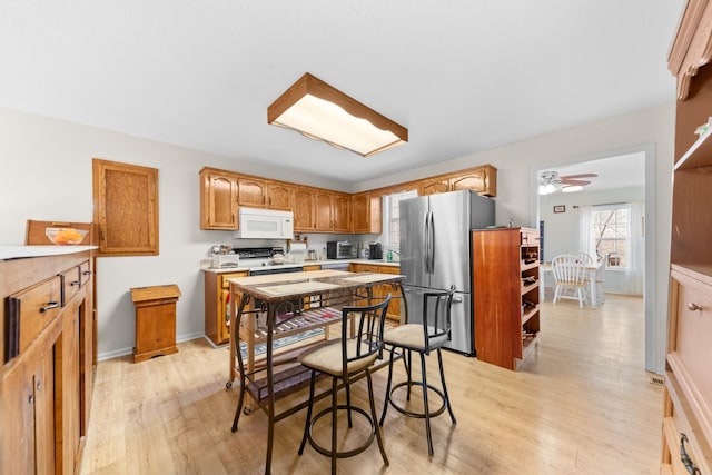 kitchen with light wood-type flooring, freestanding refrigerator, stove, and white microwave