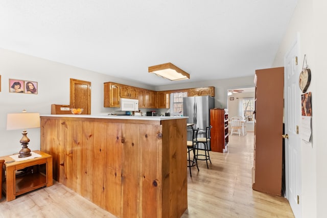 kitchen featuring light wood finished floors, light countertops, white microwave, freestanding refrigerator, and a peninsula