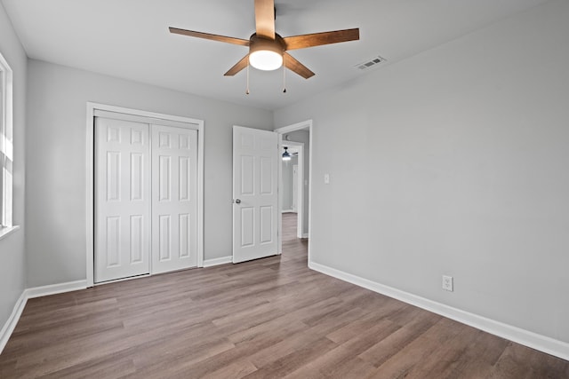 unfurnished bedroom featuring baseboards, visible vents, a ceiling fan, wood finished floors, and a closet