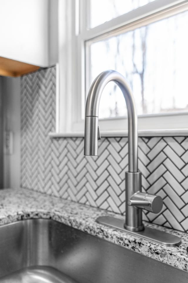 interior details with tasteful backsplash, white cabinetry, a sink, and light stone countertops