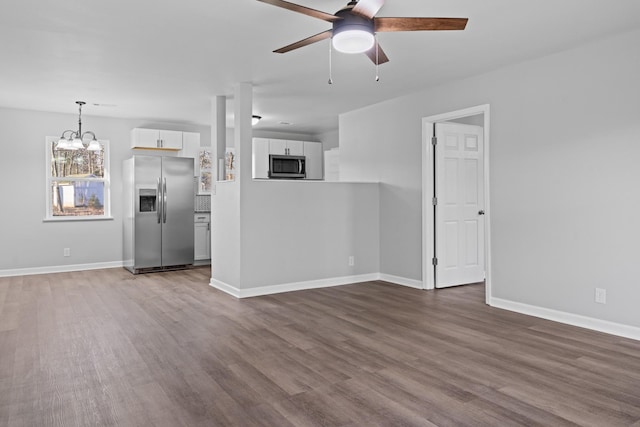 unfurnished living room with ceiling fan with notable chandelier, dark wood-style flooring, and baseboards