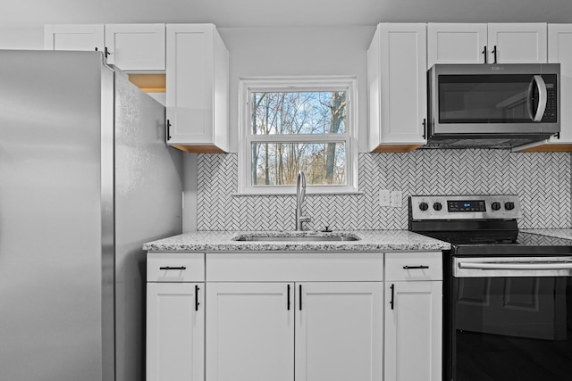 kitchen with light stone counters, stainless steel appliances, a sink, white cabinetry, and backsplash