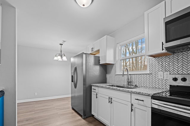 kitchen featuring light stone counters, a sink, white cabinets, appliances with stainless steel finishes, and light wood finished floors