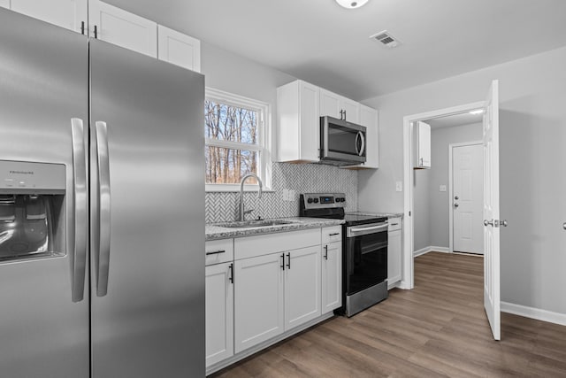 kitchen featuring decorative backsplash, appliances with stainless steel finishes, white cabinets, a sink, and wood finished floors