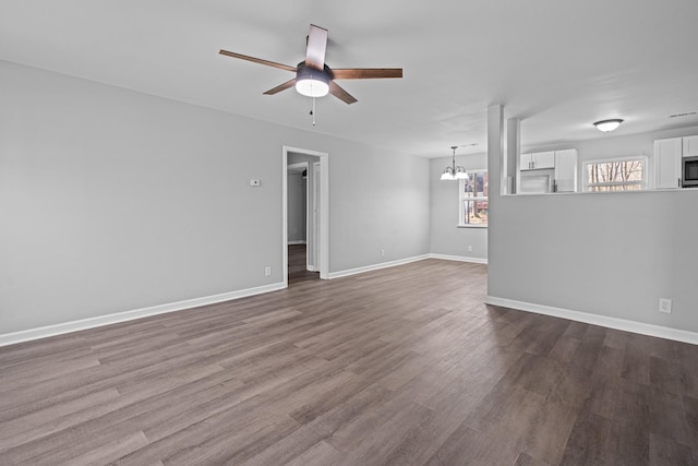 unfurnished living room featuring ceiling fan with notable chandelier, baseboards, and wood finished floors