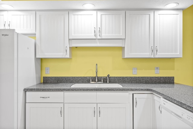 kitchen with dark countertops, white appliances, white cabinetry, and a sink