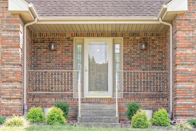 view of exterior entry featuring brick siding and roof with shingles