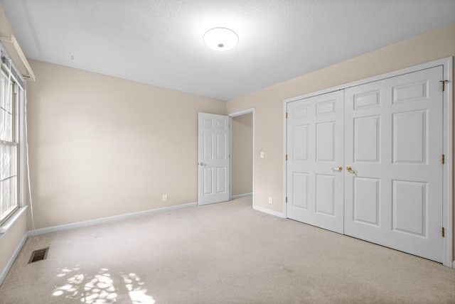 unfurnished bedroom featuring carpet, a closet, visible vents, a textured ceiling, and baseboards