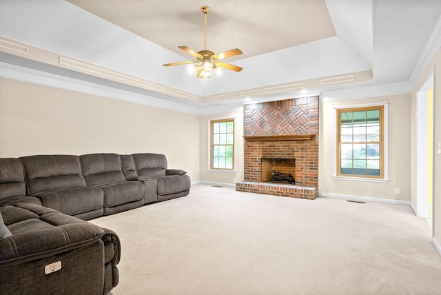 carpeted living room with ornamental molding, a brick fireplace, a raised ceiling, and baseboards