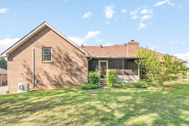 back of house featuring ac unit, brick siding, a yard, a chimney, and a sunroom