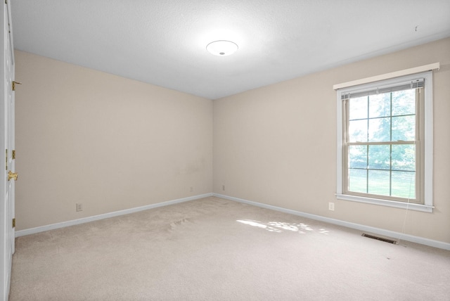 empty room featuring light carpet, visible vents, and baseboards