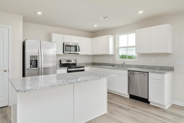 kitchen with visible vents, a kitchen island, light wood-style flooring, white cabinets, and stainless steel appliances