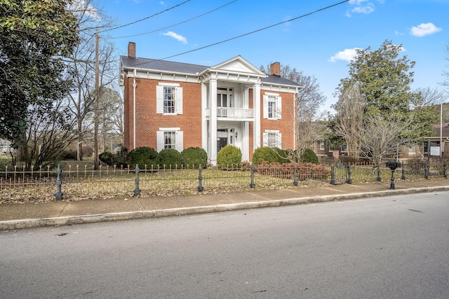 greek revival inspired property with a fenced front yard, a chimney, brick siding, and a balcony