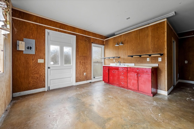 kitchen with concrete flooring, wood walls, a sink, baseboards, and electric panel