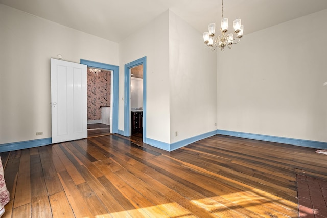 empty room featuring wood-type flooring, baseboards, and a notable chandelier