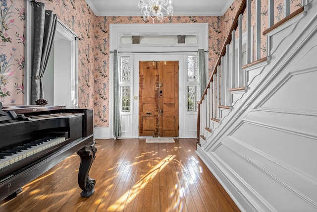 entrance foyer with wallpapered walls, a notable chandelier, stairway, and hardwood / wood-style flooring