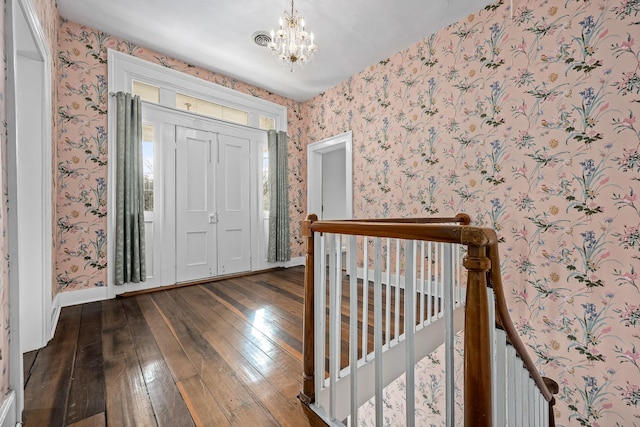 foyer featuring dark wood-style floors, an inviting chandelier, and wallpapered walls