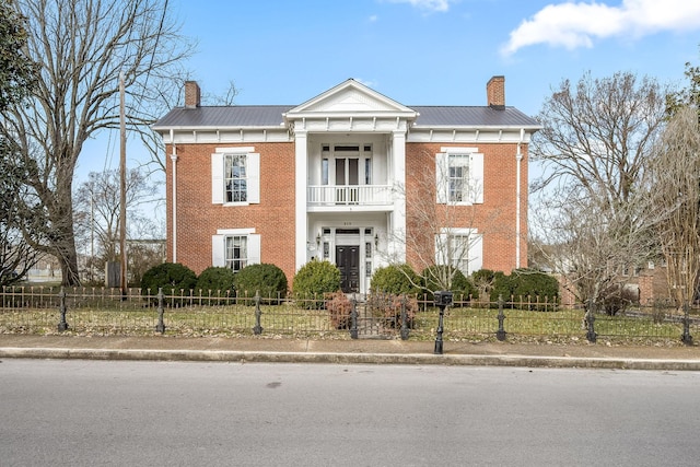 greek revival house with metal roof, a chimney, and a balcony