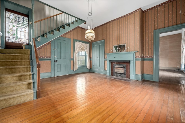 unfurnished living room featuring stairs, hardwood / wood-style flooring, a fireplace, and an inviting chandelier