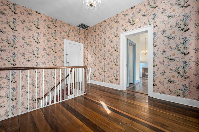 unfurnished room with wallpapered walls, baseboards, visible vents, wood-type flooring, and a chandelier