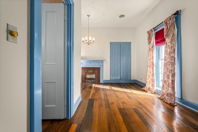 hallway with hardwood / wood-style flooring, baseboards, visible vents, and an inviting chandelier