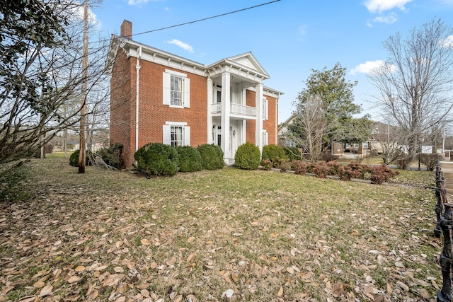 neoclassical home with brick siding, a chimney, a front lawn, and a balcony