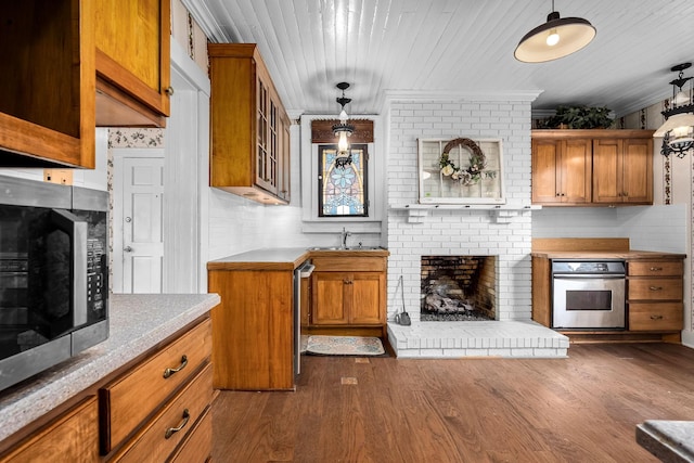 kitchen featuring brown cabinetry, wood ceiling, appliances with stainless steel finishes, dark wood-style flooring, and a fireplace