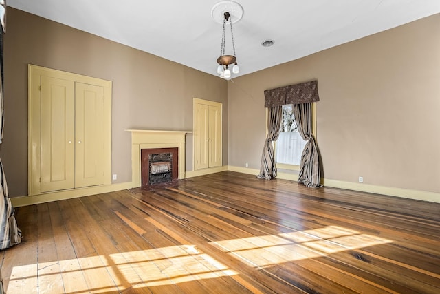 unfurnished living room featuring wood-type flooring, a fireplace, visible vents, and baseboards