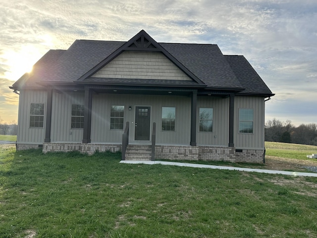 view of front facade with covered porch, a shingled roof, a front yard, and board and batten siding