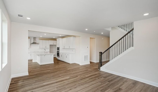 unfurnished living room with stairway, wood finished floors, visible vents, and baseboards