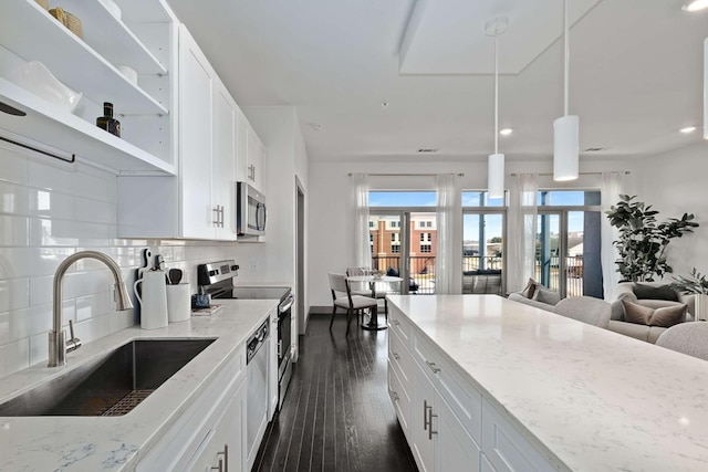 kitchen with dark wood finished floors, stainless steel appliances, decorative backsplash, a sink, and light stone countertops