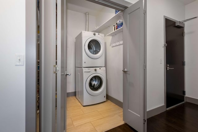 washroom featuring light wood-style floors, stacked washer and clothes dryer, baseboards, and laundry area